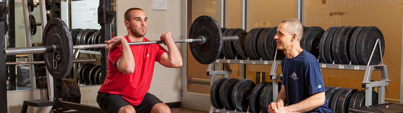 A Mount Royal trainer supervising a cleint doing a weighted front squat.