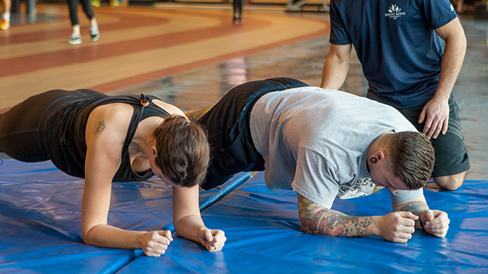 Two people holding planks while a trainer supervises.