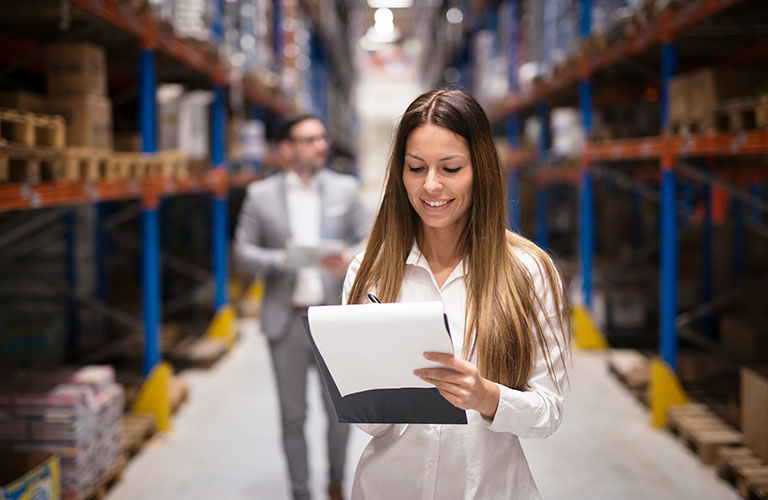 Woman writes on a clipboard in a warehouse.