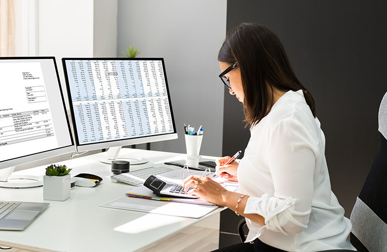 An accountant reviews accounting documents and makes calculations at her desk