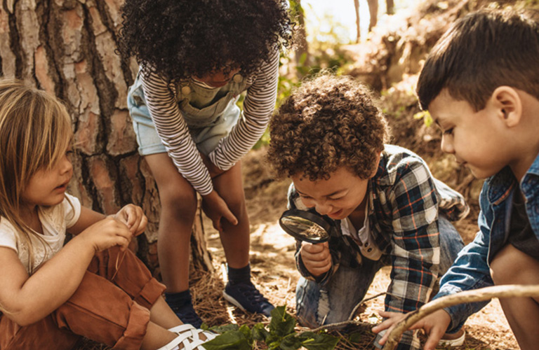 Kids in forest with a magnifying glass.