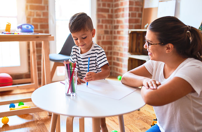 Adult woman working with child who is painting.