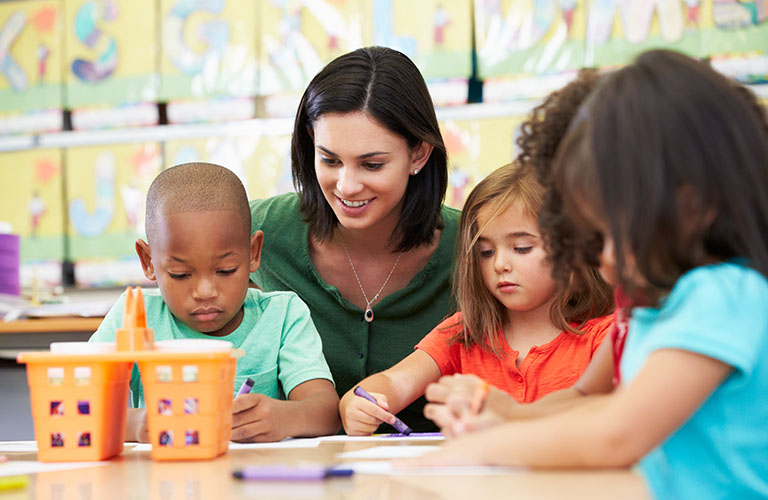 Education assistant works with three children in a classroom setting.