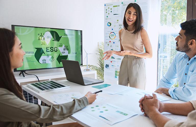 A person giving a presentation on ESG reporting to a few professionals at a table.
