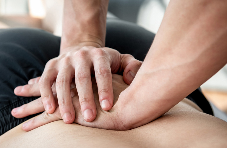 A pair of hands pressing on the pack of a person laying face down.