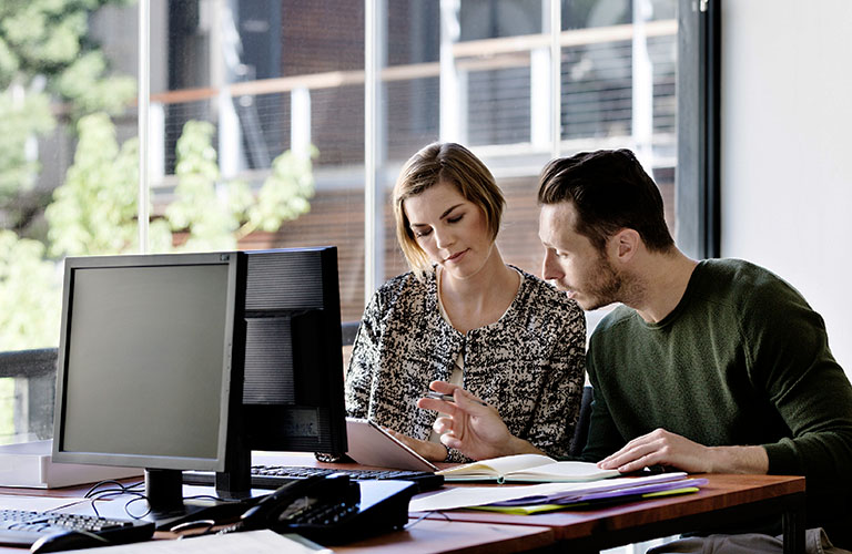 Payroll professionals review data on a computer.