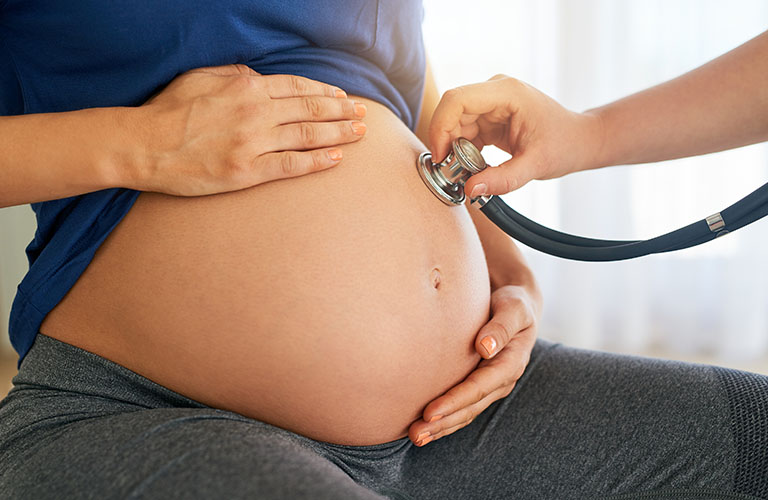 Close-up of a hand holding a stethoscope on a pregnant belly