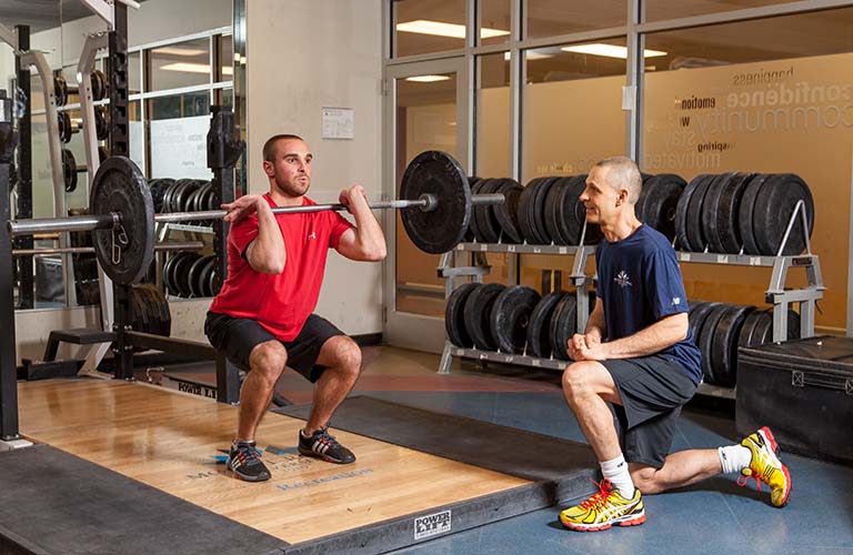 A Mount Royal trainer supervising a cleint doing a weighted front squat.