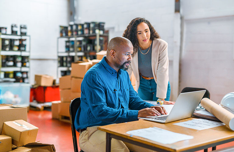 Two people looking at a laptop screen in a room with well stocked shelves.