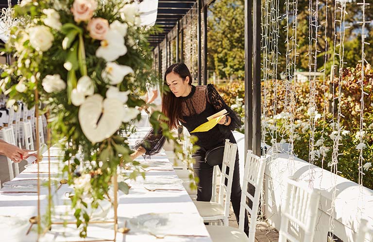 A woman adjusting the placement of cutlery on a long table full of place settings.