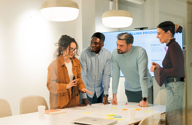 Four colleagues are discussing selling products during a business meeting in a modern office.