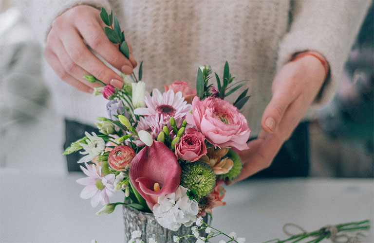 Hands placing a leafy stem into a bouquette of flowers.