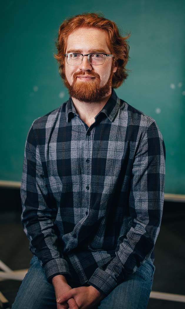 Ethan Ward sitting on a stool in front of a chalkboard.