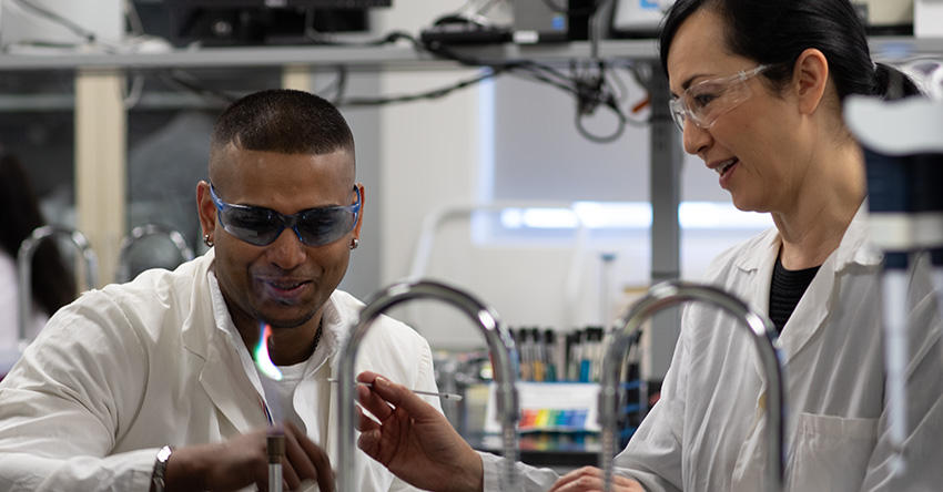 A faculty member instructing a student in a chemistry lab.