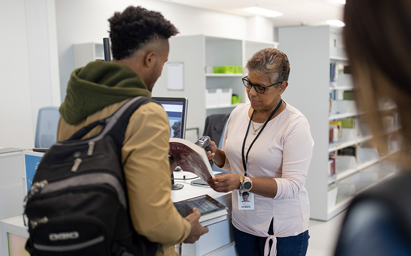 An Mount Royal University employee checks out a book for a student.