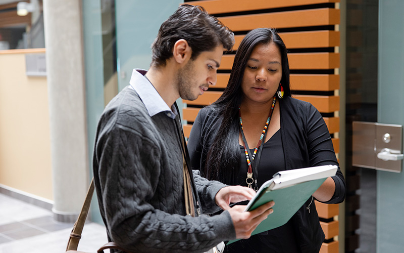 Two professionals in the Roderick Mah Centre for Continuous Learning discussing notes in a notebook.