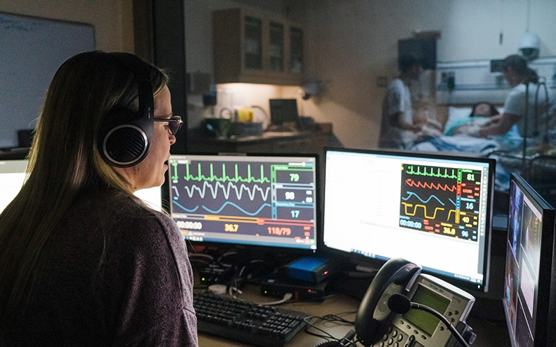 A medical tech supervising nursing students practicing clinic skills on a simulation dummy in the Health Simulation Learning Centre.