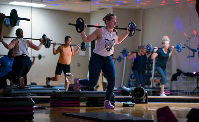 A group of people in althetic attire lifting weighted barbells as part of a fitness class.
