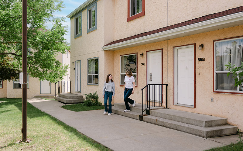 Two students exiting a townhouse on a sunny summer day.