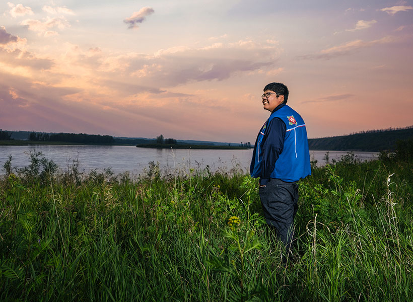 Samuel Metacat-Yah looking out over a river and fiery sunset.