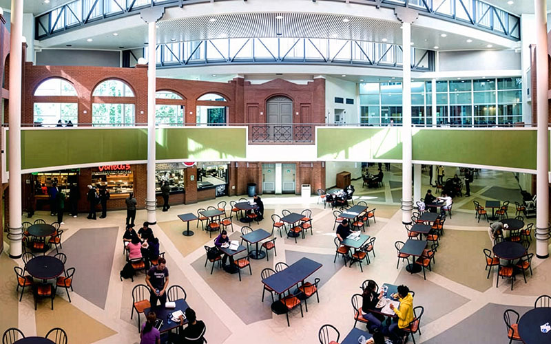 An atrium of a building with brick and glass features, looking down on a food court from a second floor balcony.