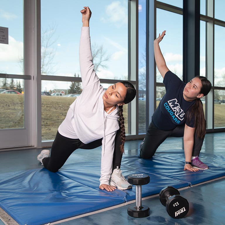 Two Indigenous students stretching in Mount Royal's recreation centre.