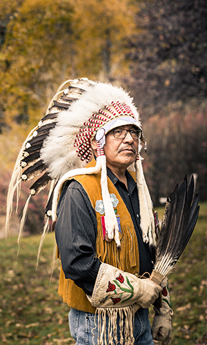 Elder Miiksika'am in full Indigenous regalia by the Mount Royal University's Charleton Pond.