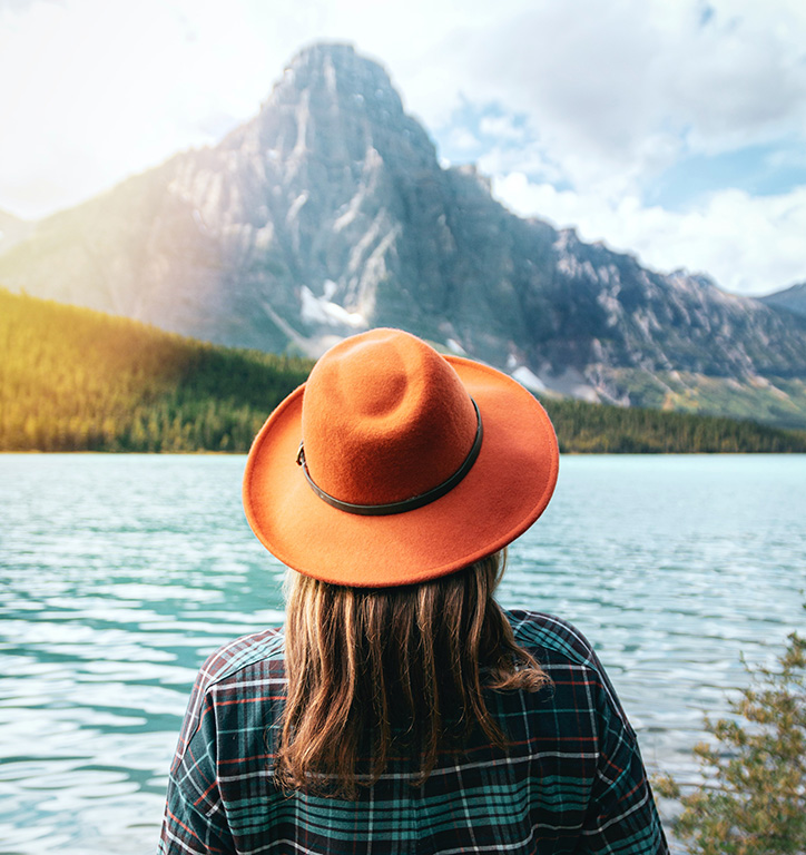 A woman in a wide brimmed hat enjoying a view of a mountain lake and mountain peak.