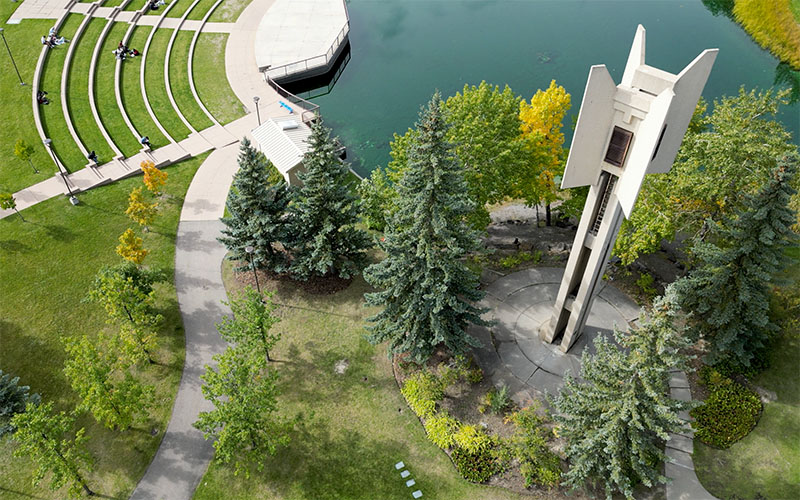 Aerial shot of the Kerby Memorial Tower, a concrete twoer with four decorative wings, placed beside the Charlton Pond and surrounded by trees and bushes.