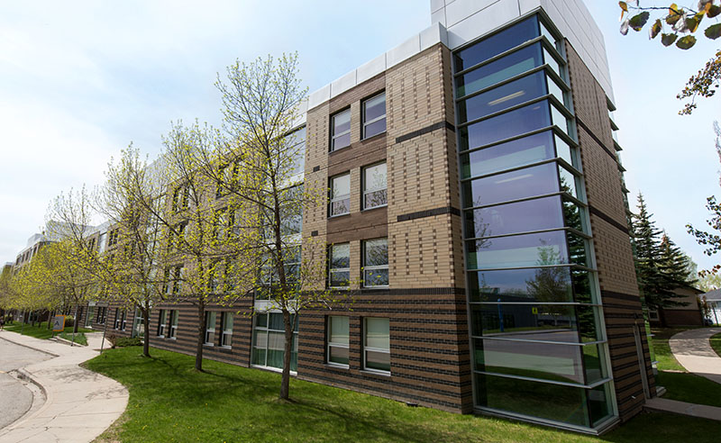 Outside of West Residence on a spring day - the building is made of glass and several tones of brown bricks.