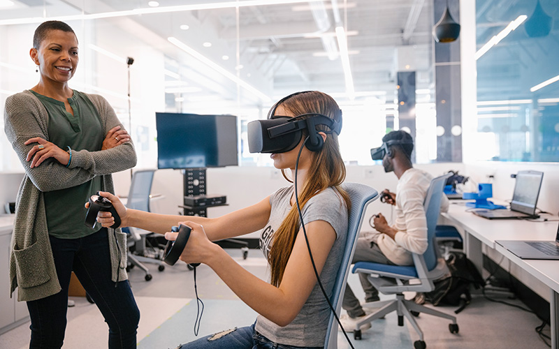 Two students using VR goggles while supervised by an employee in the Riddell Library and Learning Centre's VR Lab.