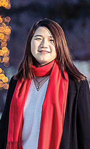 A winter scene of international student Vidal Zhou standing in front of trees decorated with lights.