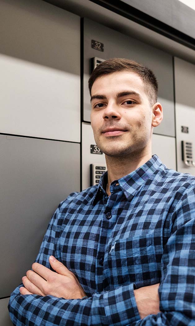 Esthevan Machado, arms crossed and smiling in front of a row of small lockers.