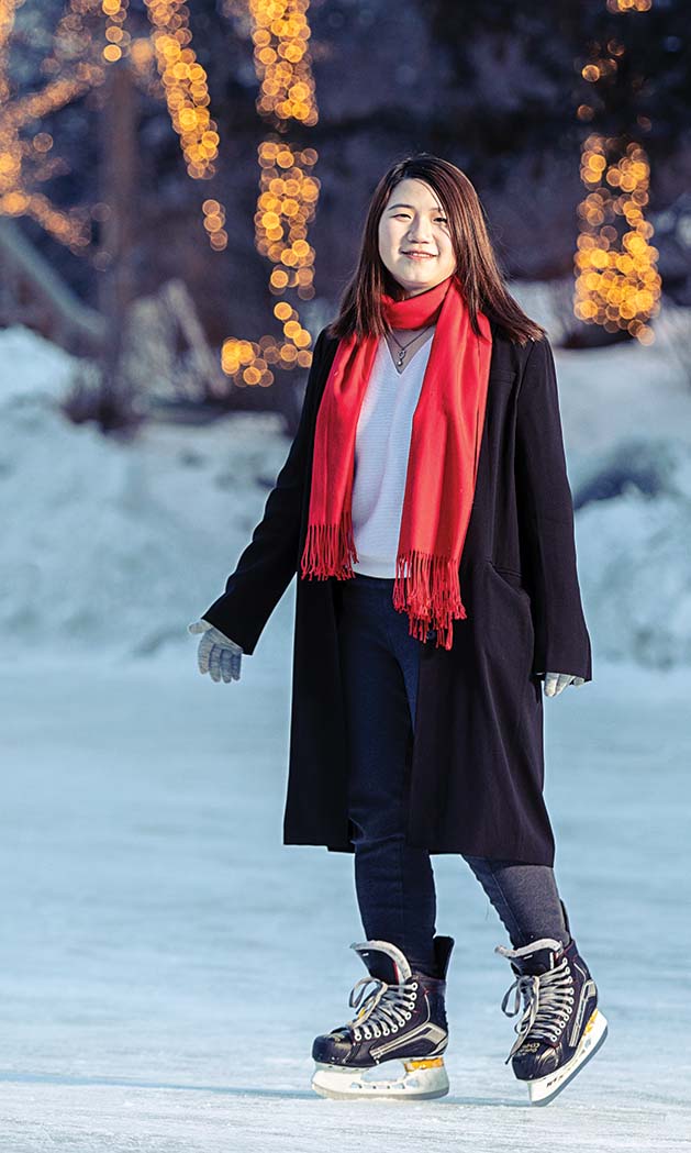 A winter scene of international student Vidal Zhou standing in front of trees decorated with lights.