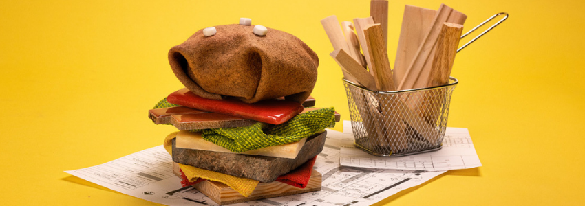 A hamburger and a cup of fries made from a blend of fabric and wood placed on a table.