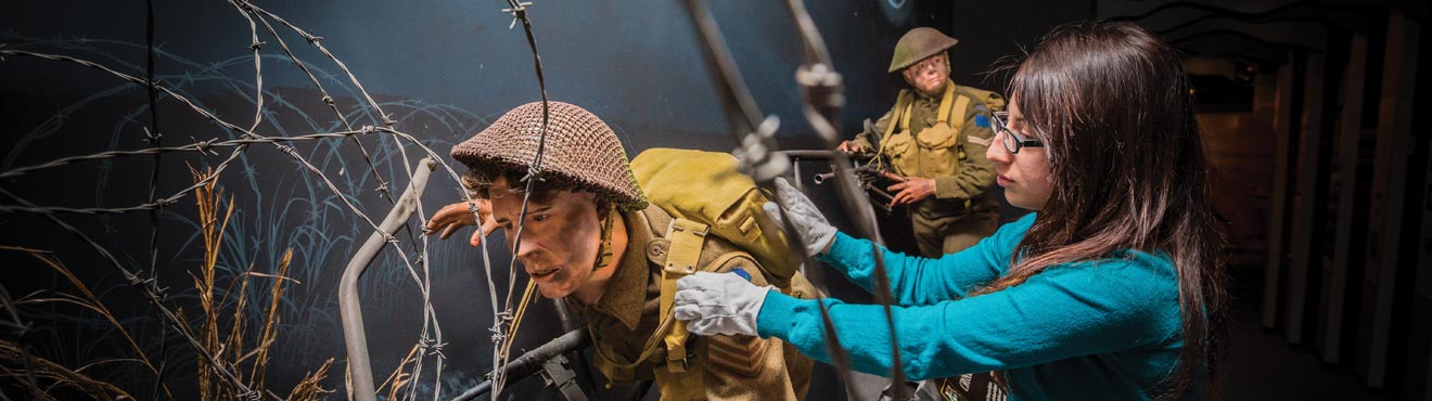 A museum professional make adjustments to a military display.