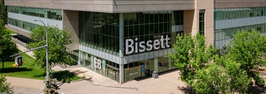 Exterior view of the Bissett School of Business building at dusk, featuring a multi-story illuminated glass atrium with a small red aircraft suspended inside.