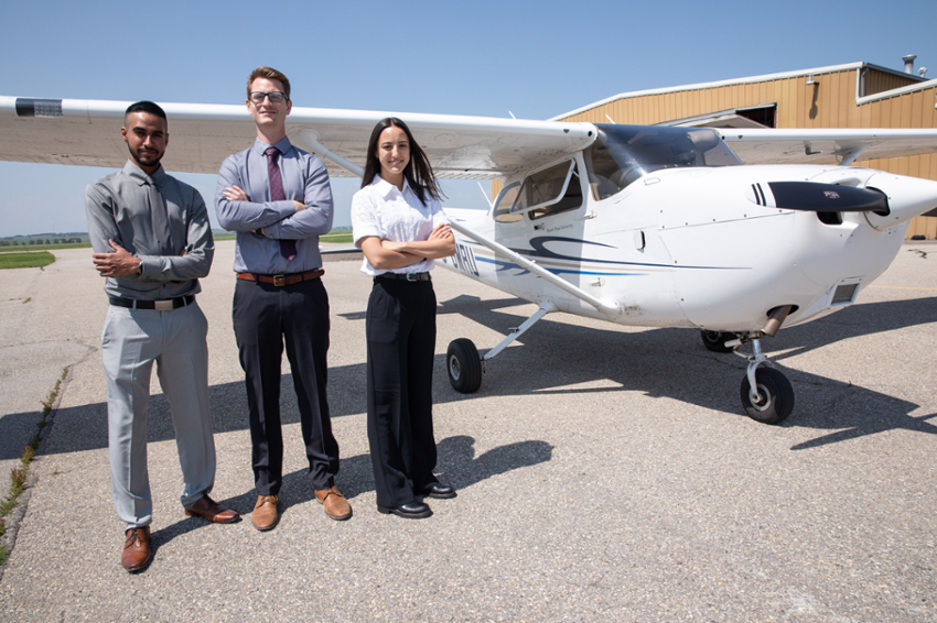 Three students standing in front of a Mount Royal Univeristy Cessna at the Springbank Hangar.