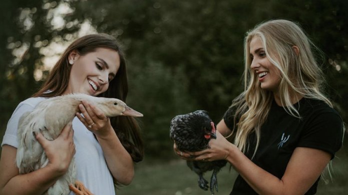 Taylor Pelland, left, holding a white duck and her sister, Quinn Pelland, holding a black chicken.