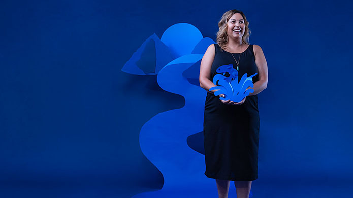 Photo of Jenny Philbrick in front of a blue backdrop holding a paper sculpture.