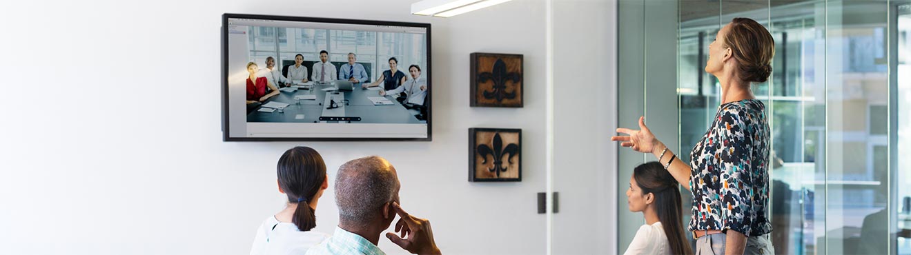 A group of business professionals in a meeting room talking to people via video conference.