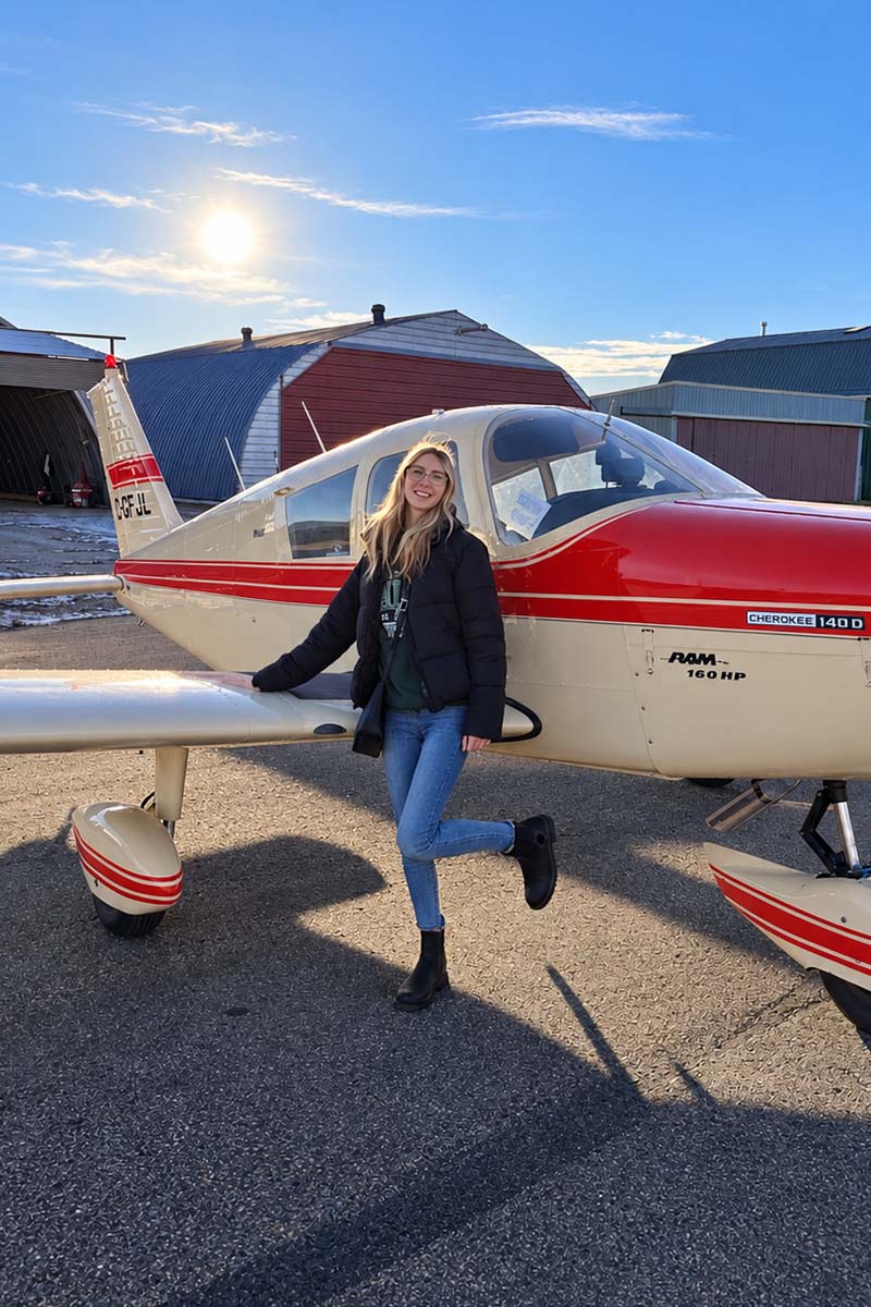 Emily Pendrak standing in front of a Piper PA-28-140D Cherokee plane.