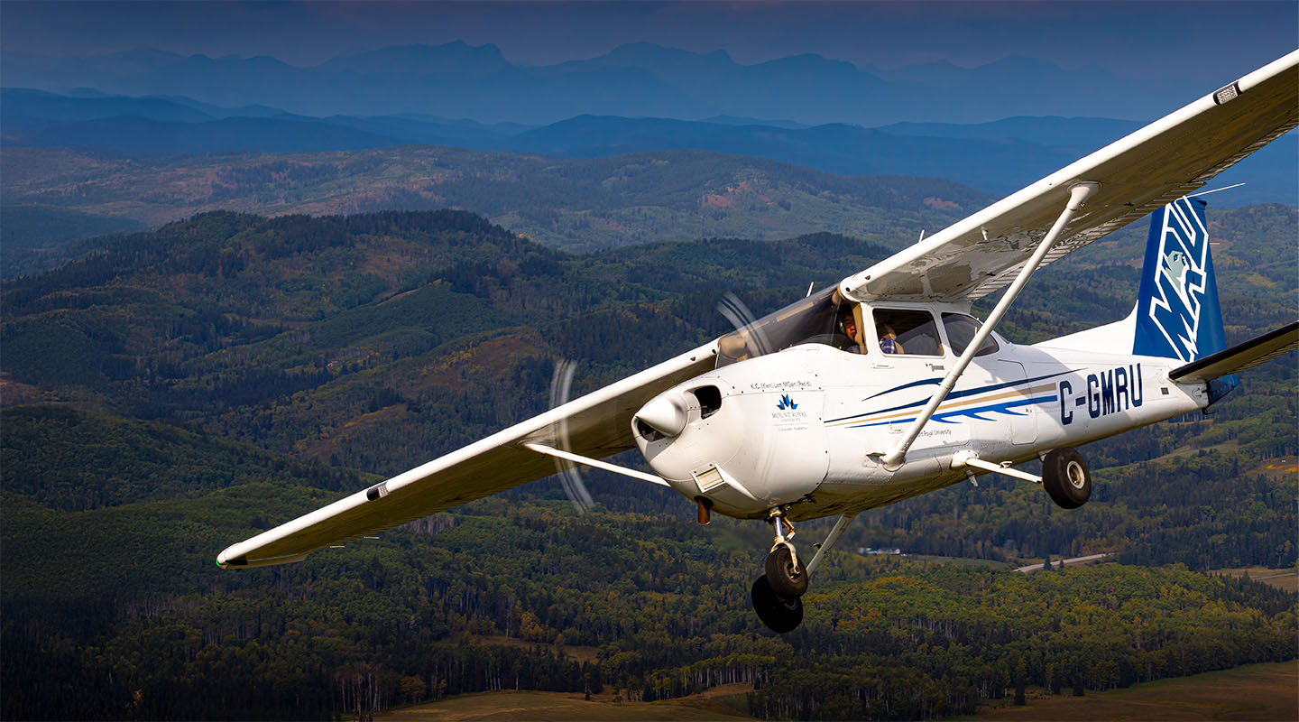 MRU-branded plane flying in framed by the Rocky Mountains.