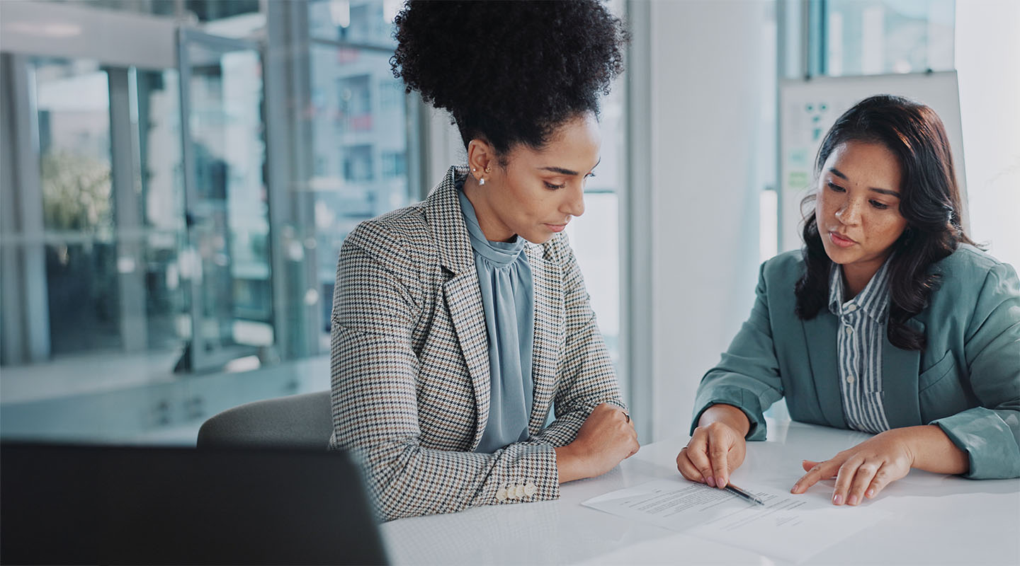 Two professionals in a meeting room reviewing a document.