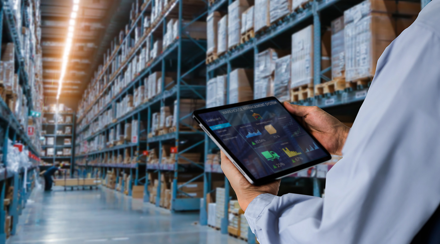A professional reviewing charts on a tablet while in the aisle of a well-stocked warehouse.