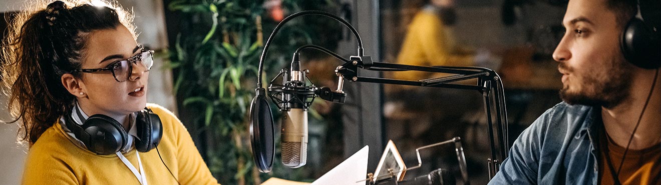 Two young people having a conversation in a radio station recording booth.