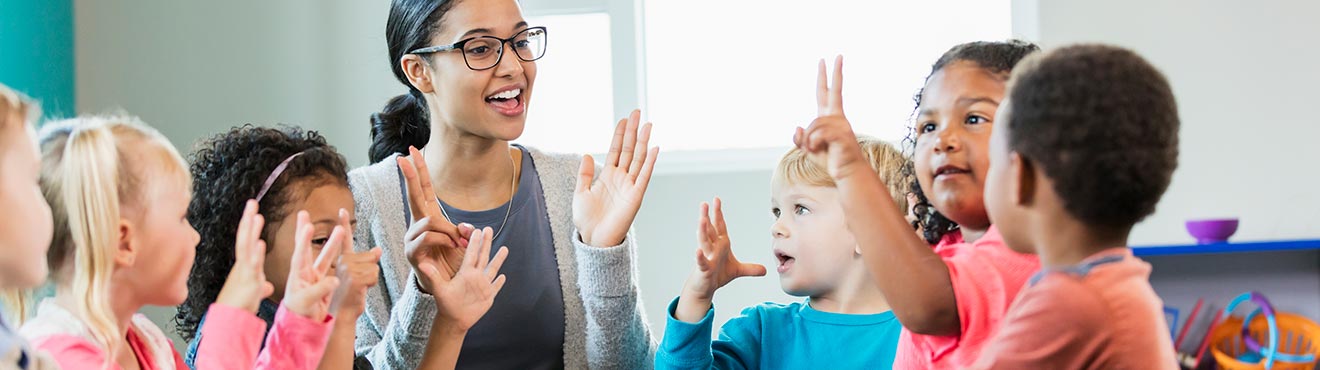 Mixed race woman holding up two fingers while a group of children immitate her.