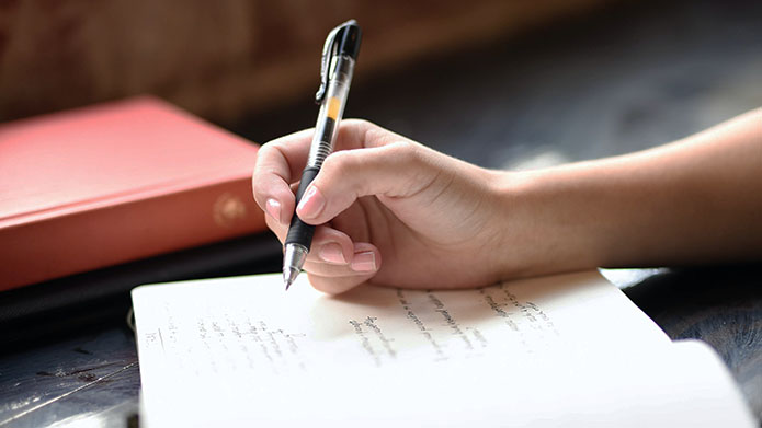 Photo of a hand writing in a journal.