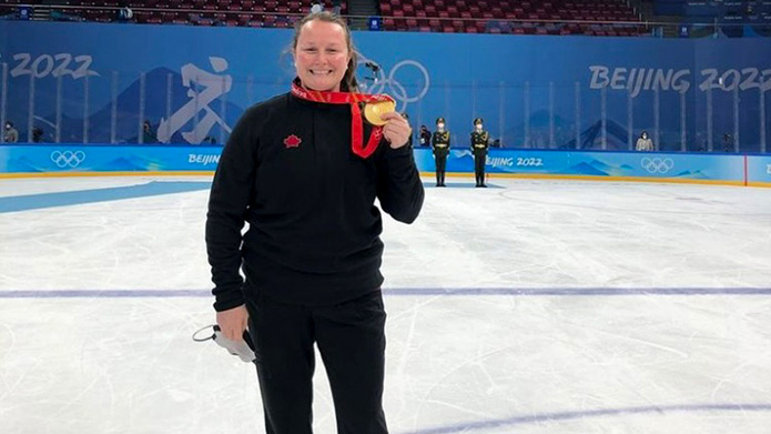 Alumna Christine Atkins stands on the ice in a hockey rink holding a gold olympic medal