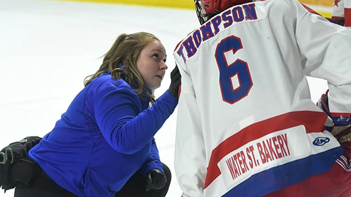 Alumna Christine Atkins stands on the ice in a hockey rink holding a gold olympic medal